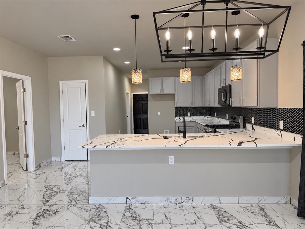 Kitchen featuring stone-patterned tile flooring, a peninsula with stone-look countertop, herringbone-patterned tile backsplash, and decorative pendant and chandelier lighting Kitchen featuring stone-patterned tile flooring, a peninsula with stone-look countertop, herringbone-patterned tile backsplash, and decorative pendant and chandelier lighting