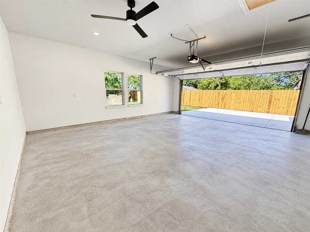 Two-car garage featuring a smooth concrete floor, dual windows, matte black ceiling fan, and automated garage door opener