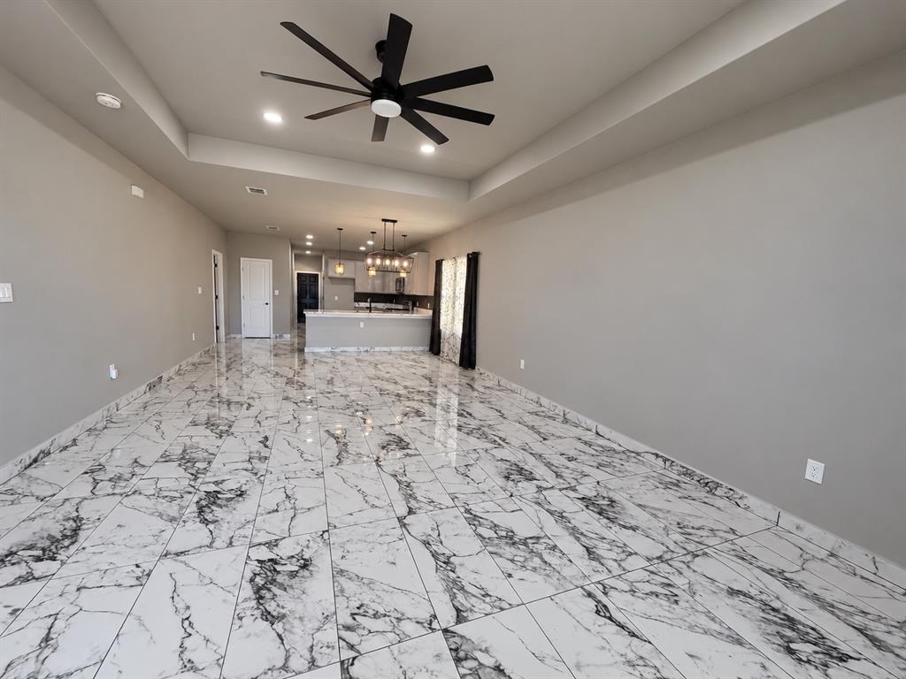 Large open area featuring a tray ceiling, matte black multi-blade ceiling fan, recessed lighting, and polished stone-finish tile flooring Large open area featuring a tray ceiling, matte black multi-blade ceiling fan, recessed lighting, and polished stone-finish tile flooring