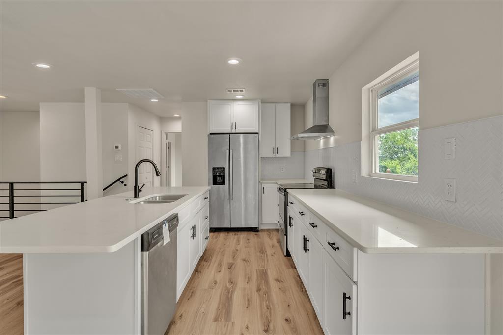 Kitchen featuring white cabinetry, quartz countertops, wood-finish flooring, a stainless steel range hood, and a herringbone-pattern backsplash Kitchen featuring white cabinetry, quartz countertops, wood-finish flooring, a stainless steel range hood, and a herringbone-pattern backsplash