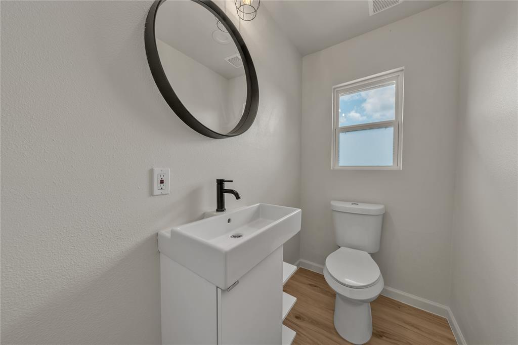 Modern white pedestal vanity with matte black faucet, circular black-framed mirror, and wood-finish flooring