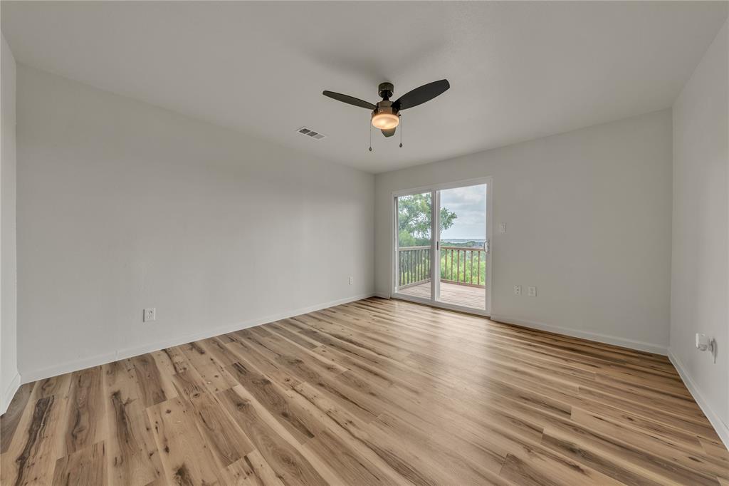 Room featuring wood-finish flooring, a ceiling fan with integrated lighting, and a sliding glass door providing external access to a wooden deck