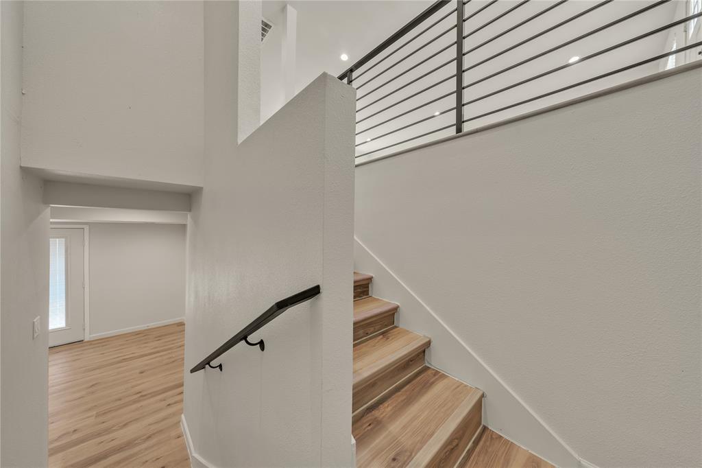 Staircase featuring wood-finish treads, a dark metal handrail, and a metal horizontal-bar railing