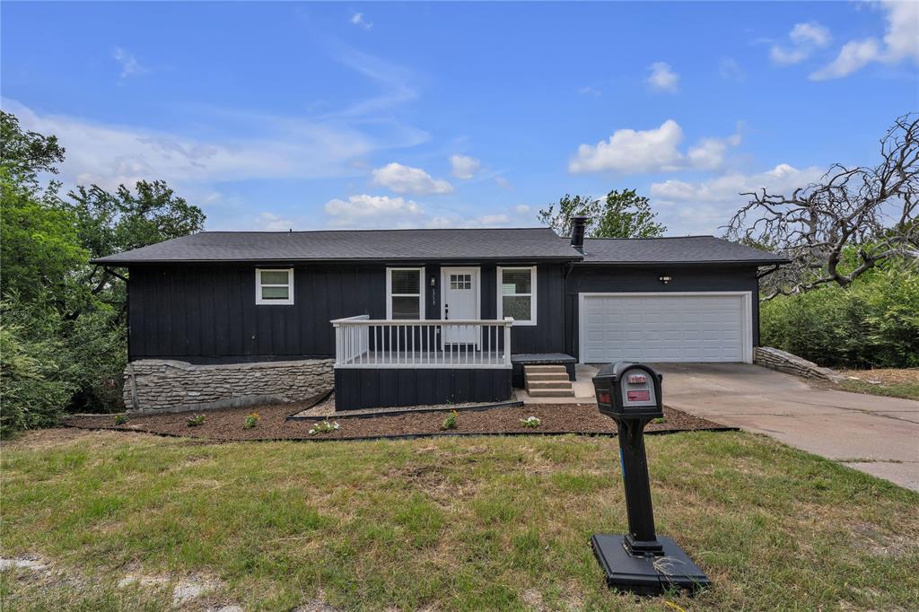 Single-story exterior featuring dark vertical siding, an attached garage, a raised deck with white railing, and a stone veneer foundation