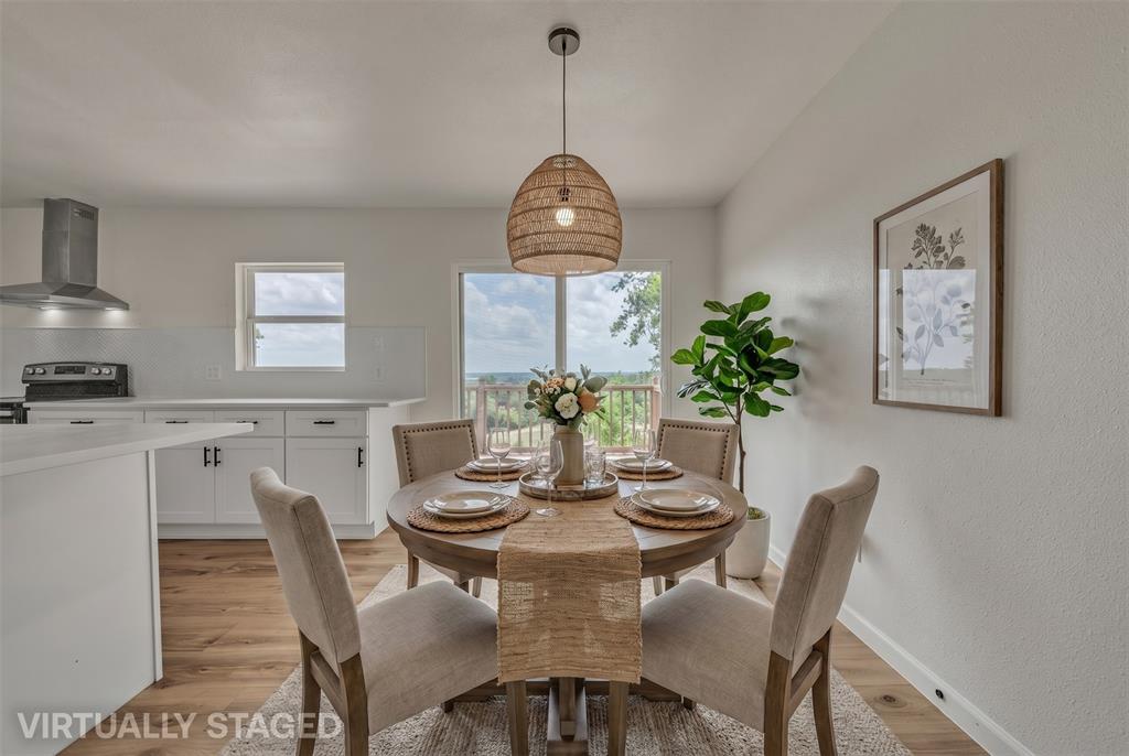 Open-concept kitchen featuring white cabinetry, a stainless steel range hood, wood-finish flooring, and a glass sliding door with exterior scenery Open-concept kitchen featuring white cabinetry, a stainless steel range hood, wood-finish flooring, and a glass sliding door with exterior scenery