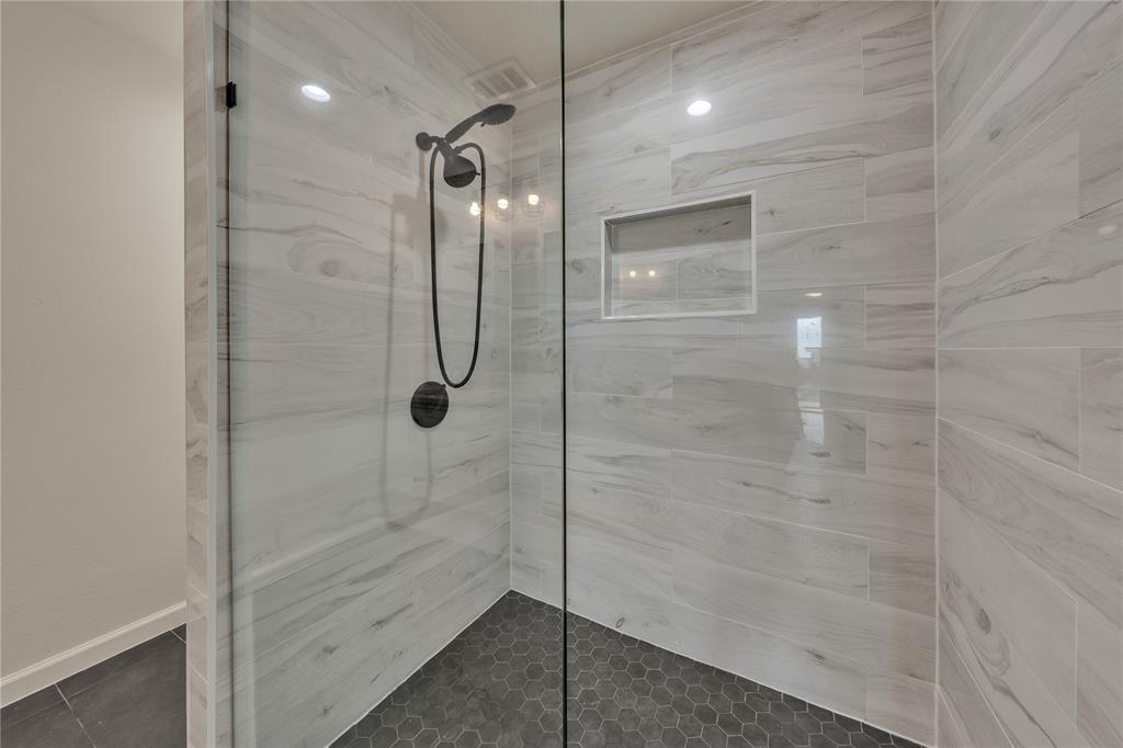 Walk-in shower featuring large-format horizontal wall tile, hexagonal floor tile, matte black plumbing fixtures, glass enclosure, and a built-in recessed wall niche
