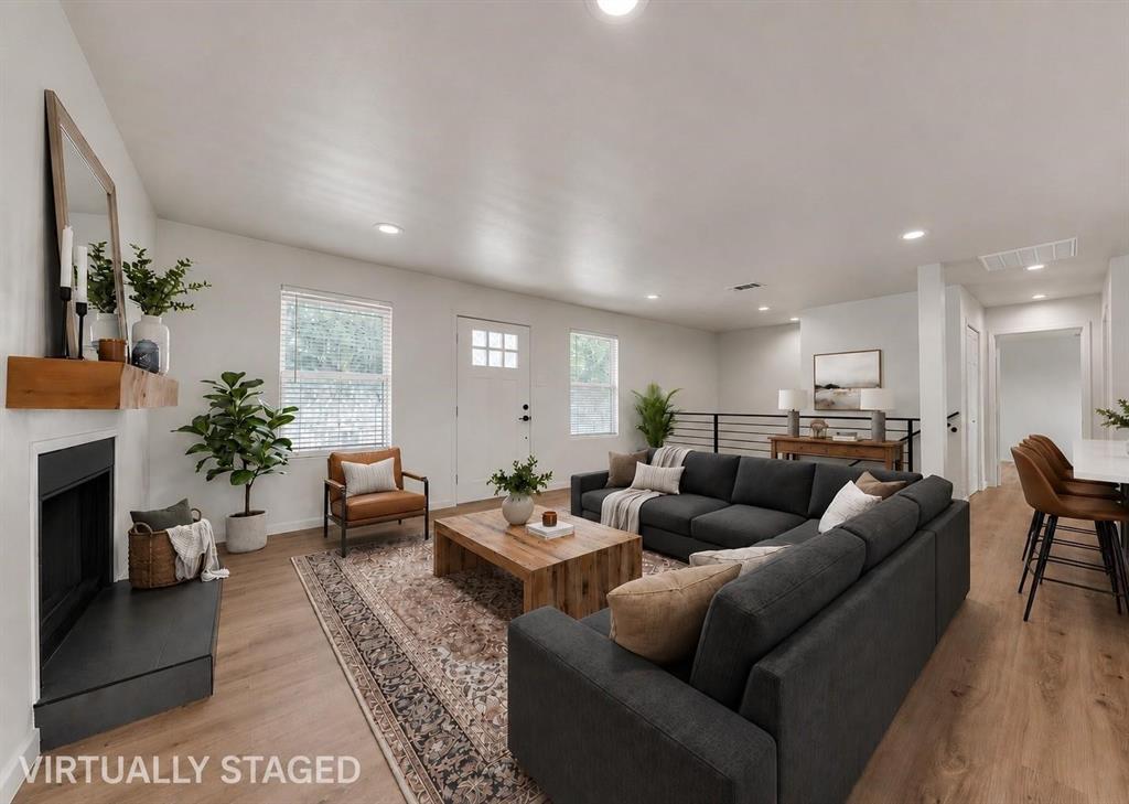 Open-concept living space featuring wood-finish flooring, recessed lighting, a fireplace with a wood mantel, and a horizontal metal railing Open-concept living space featuring wood-finish flooring, recessed lighting, a fireplace with a wood mantel, and a horizontal metal railing