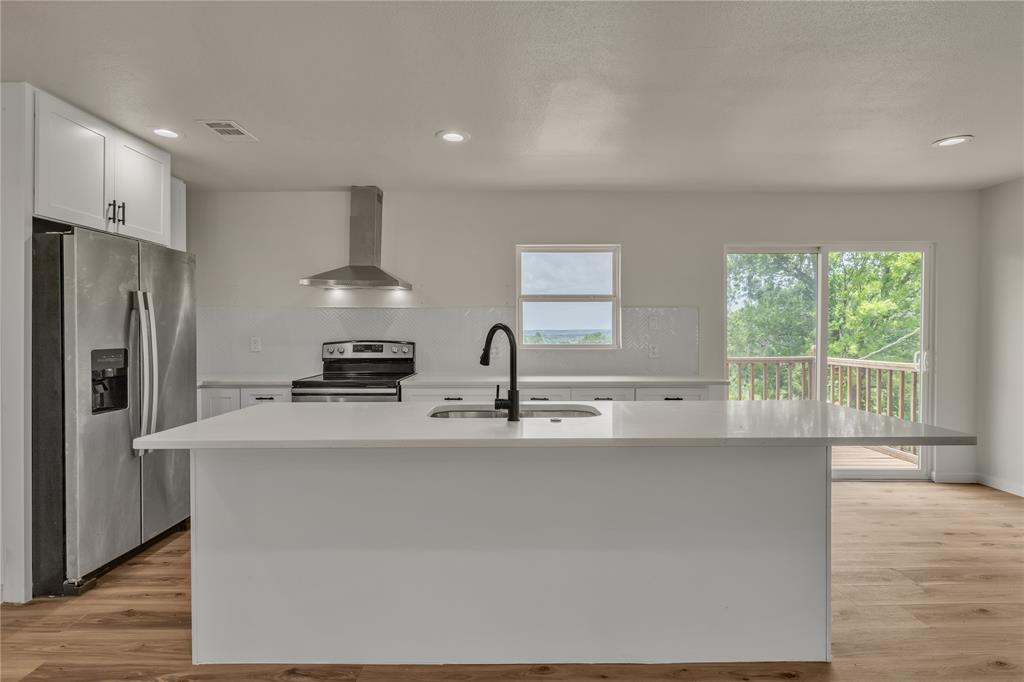 Kitchen featuring a central island with a quartz countertop, stainless steel appliances, a stainless steel range hood, matte black faucet hardware, and wood-finish flooring Kitchen featuring a central island with a quartz countertop, stainless steel appliances, a stainless steel range hood, matte black faucet hardware, and wood-finish flooring