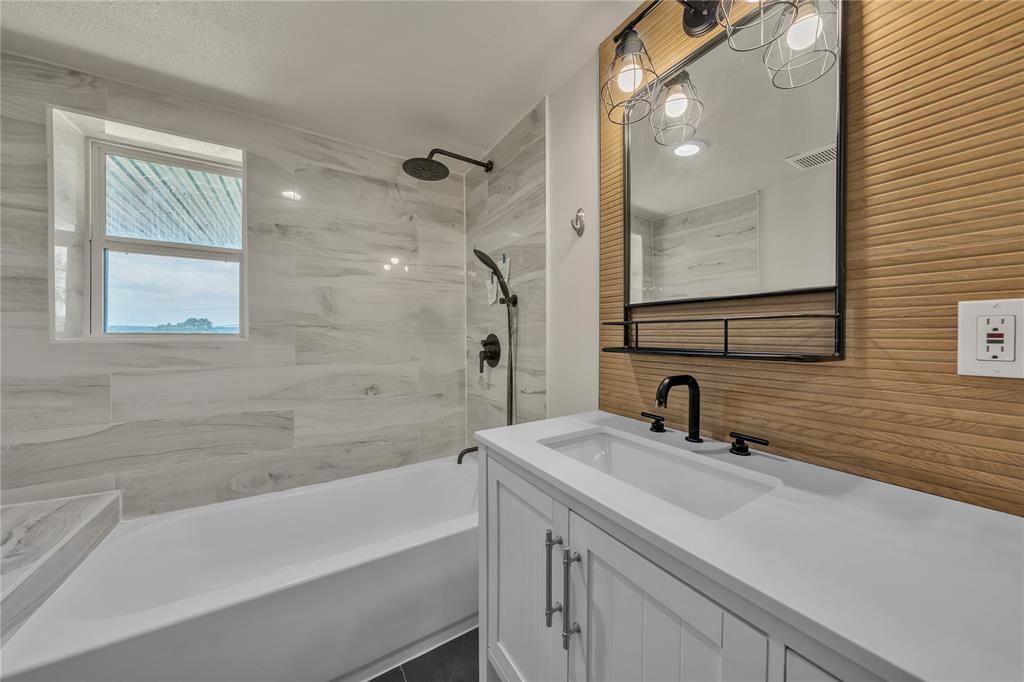 Bathroom featuring a white vanity with a rectangular basin, quartz countertop, matte black plumbing fixtures, wood-slat accent wall, and a tiled shower surround