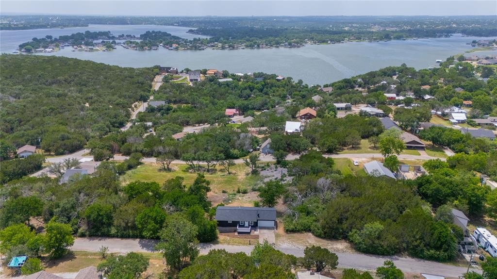 Aerial perspective showcasing a single-story residence with a dark exterior, attached garage, paved driveway, and expansive natural landscape
