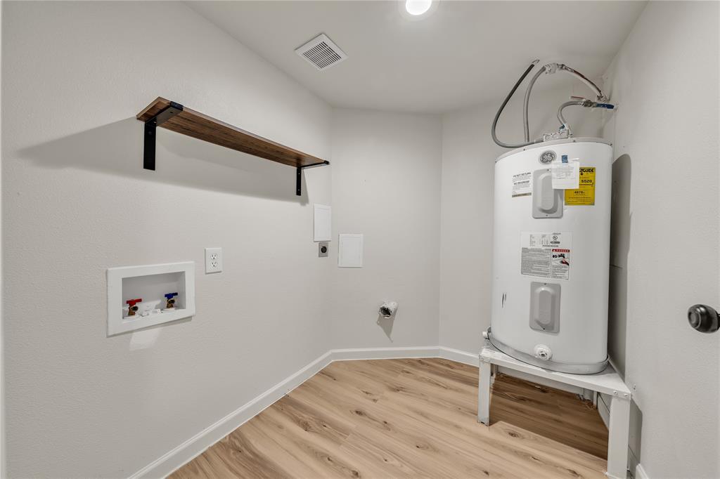 Utility space featuring wood-finish flooring, a mounted wall shelf with black metal brackets, and a recessed water supply box