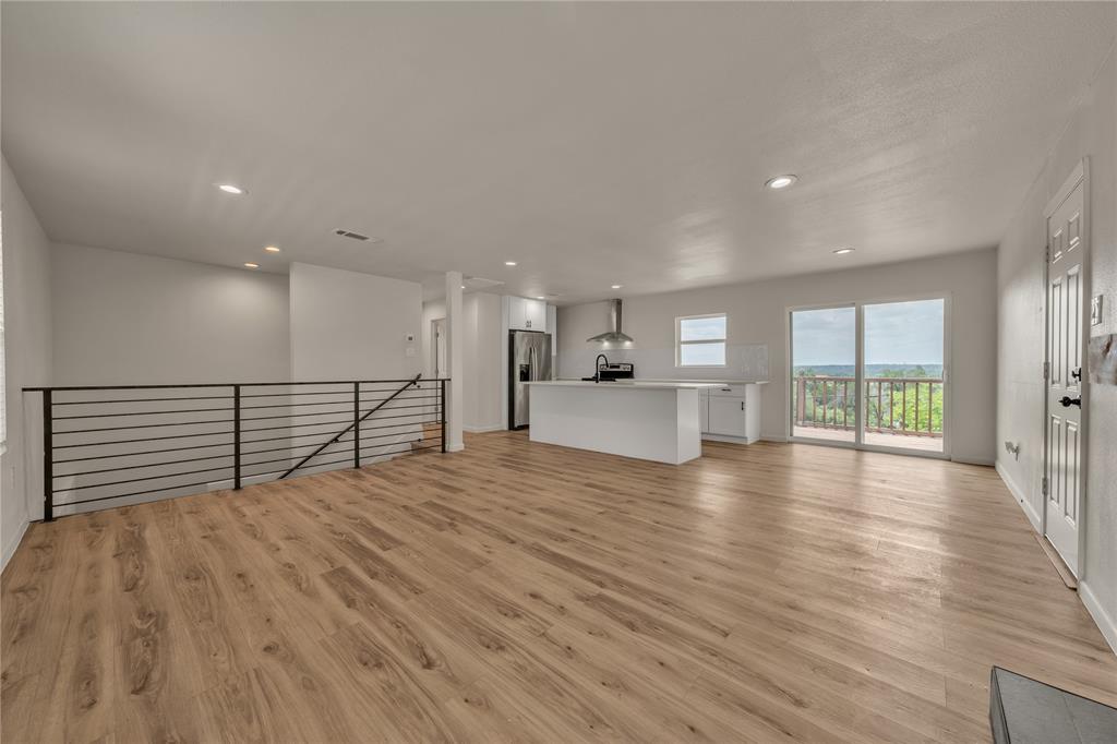 Open-concept floor plan featuring wood-finish flooring, a kitchen island with stone-finish countertops, stainless steel appliances, recessed lighting, and a metal horizontal-rail staircase Open-concept floor plan featuring wood-finish flooring, a kitchen island with stone-finish countertops, stainless steel appliances, recessed lighting, and a metal horizontal-rail staircase
