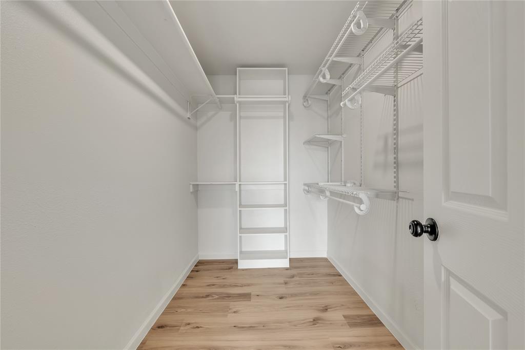 Walk-in closet featuring wood-finish flooring, white-finish wall shelving, tiered vertical built-in shelving, and wire hanging rods