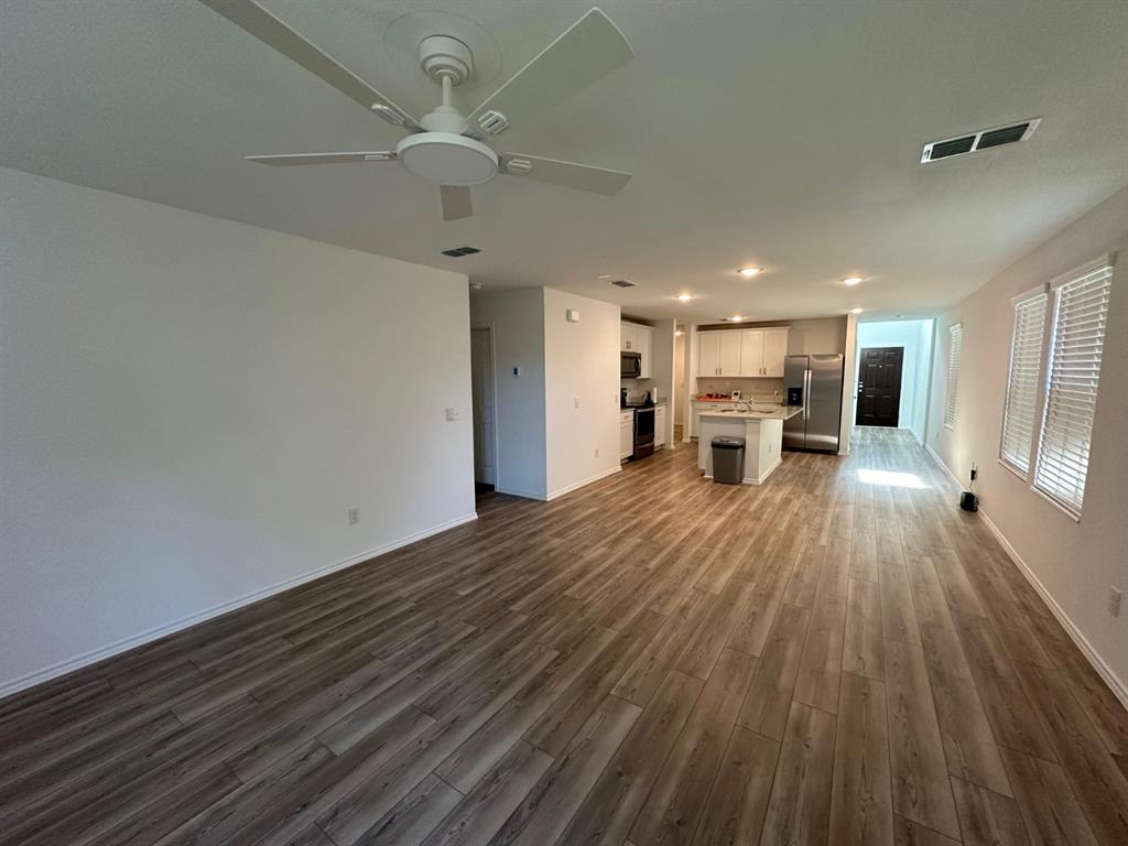 Open-concept interior featuring wood-finish flooring, a kitchen island, white cabinetry, stainless steel appliances, and a ceiling fan