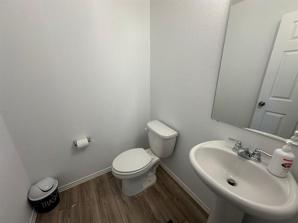 Powder room featuring wood-finish flooring, a white pedestal sink with dual-handle chrome faucet, and a wall-mounted mirror