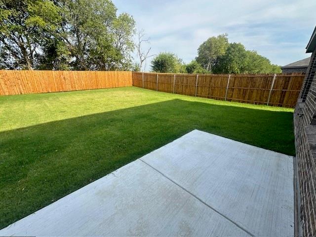 Rear exterior featuring a concrete patio, a level grass lawn, and a full-height wood perimeter fence