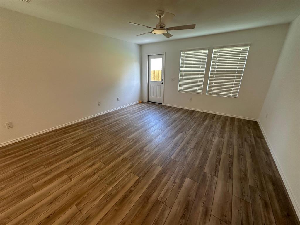 Interior room featuring wood-finish flooring, a ceiling fan with integrated lighting, dual windows with horizontal blinds, and a paneled exterior door