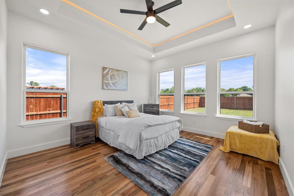 Room featuring a tray ceiling with recessed lighting, wood-finish flooring, a matte black ceiling fan, and large windows