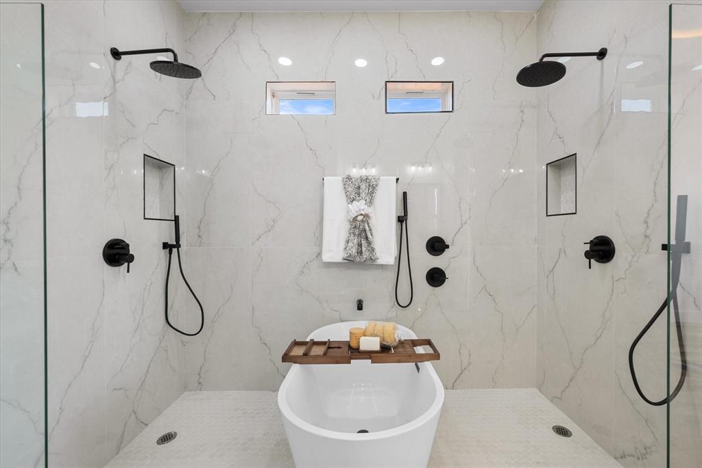 Walk-in wet room featuring a freestanding soaking tub, dual rainfall showerheads, matte black fixtures, built-in wall niches, and floor-to-ceiling stone-look tiling