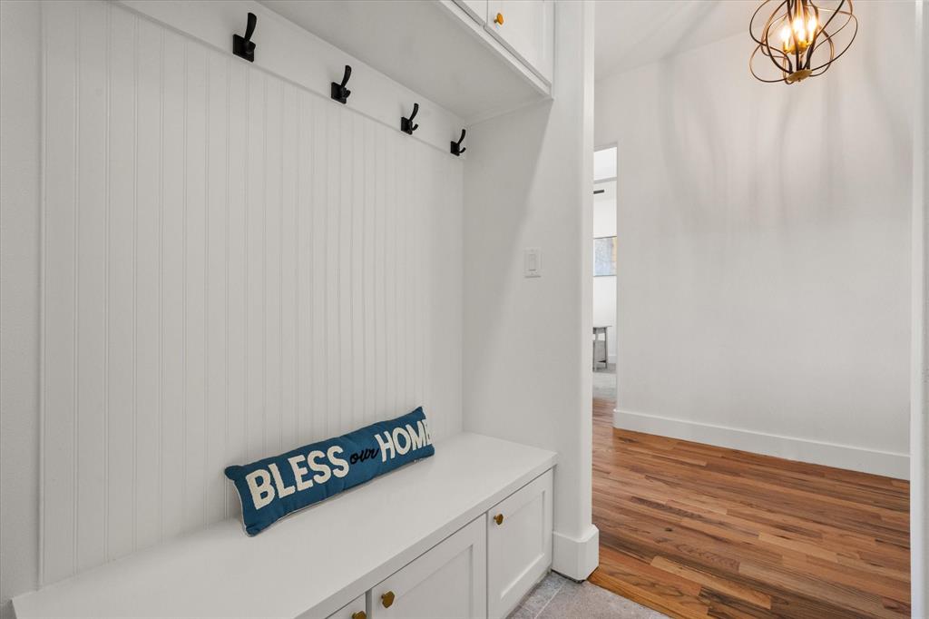 Built-in mudroom bench with beadboard paneling, matte black wall-mounted coat hooks, overhead cabinetry, and Oak wood flooring
