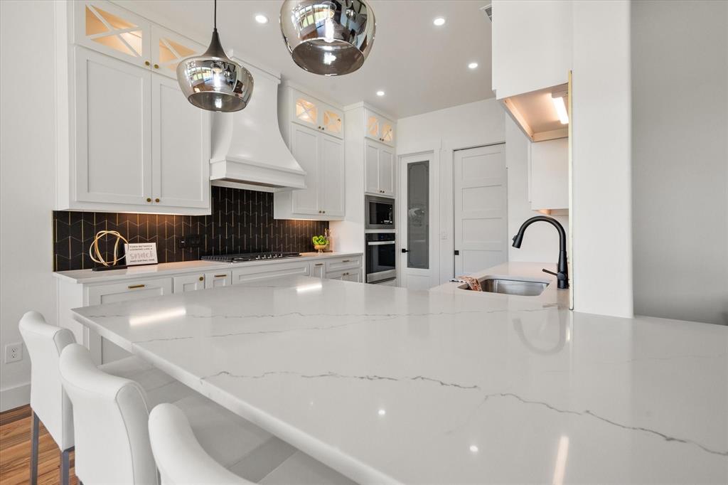 Quartz countertops with a black-gold tiled backsplash, 42" cabinets with upper cabinets with glass inserts and lighting