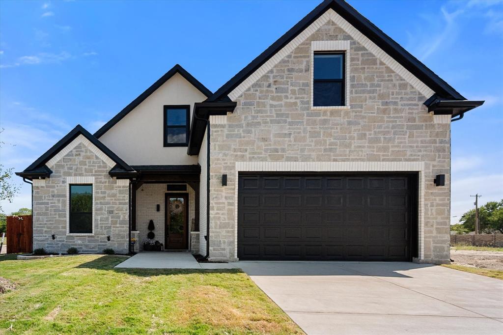 Exterior featuring stone, stucco and brick with a multi-gabled roofline, extra wide concrete driveway, and attached two-car garage
