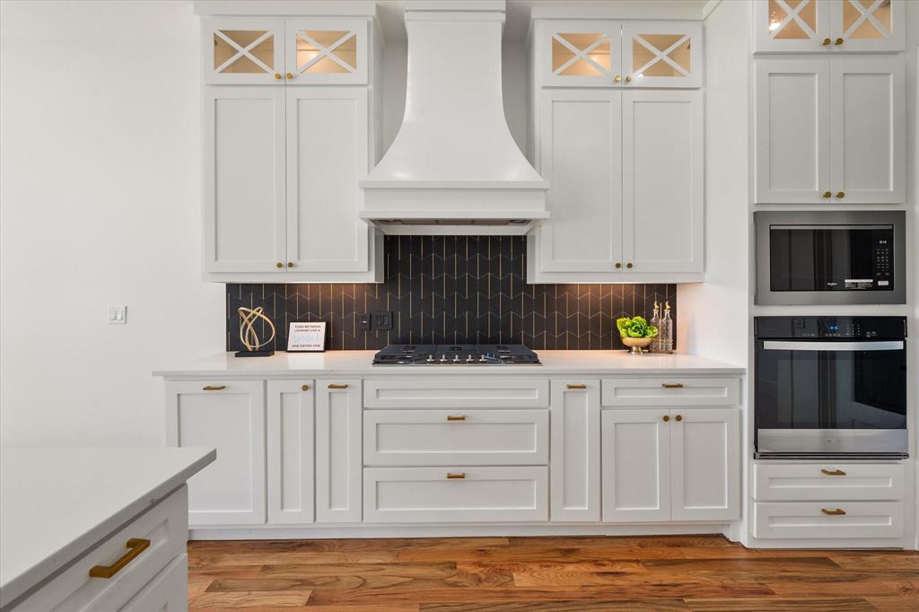 Custom designed hood and modern black/gold tiled backsplash and a 5 burner gas stove. Electric Whirlpool oven and built in microwave