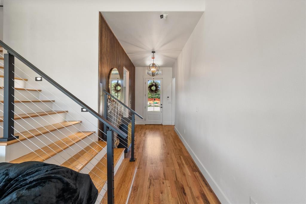 Foyer featuring wood-finish flooring, a wood-slat accent wall, a staircase with cable railing, and a decorative orb-style pendant light fixture