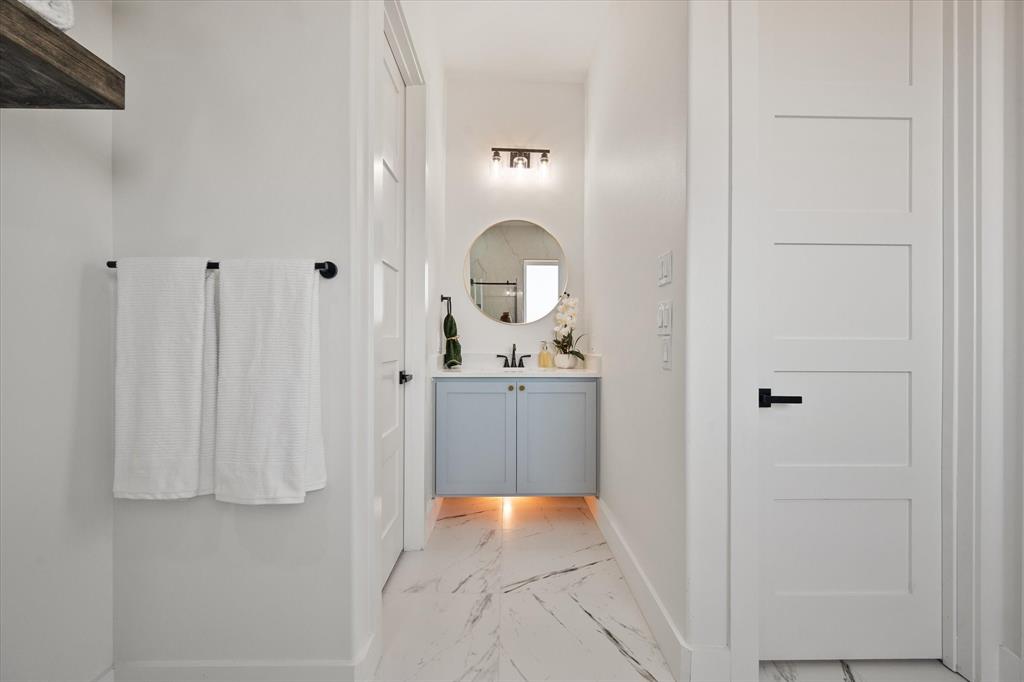 Mother in law ensuite bathroom with a floating vanity with  cabinet and solid Quartz countertop, round mirror, three-light matte black vanity fixture, and large-format tile flooring with marble-finish veining