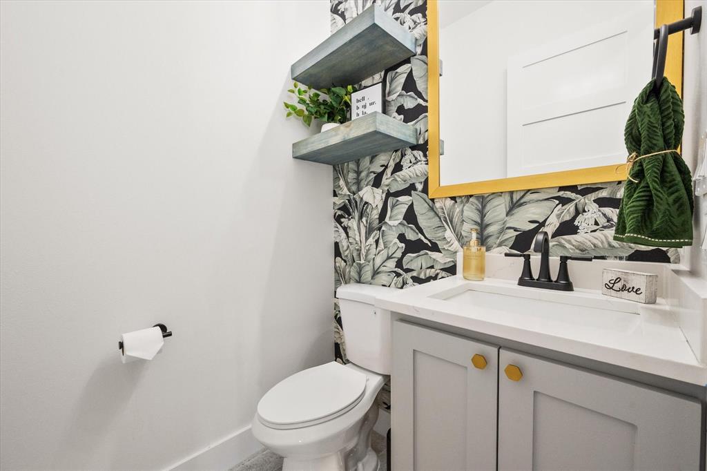 Hallway half bathroom with a shaker-style floating vanity with a Quartz countertop, matte black faucet, gold-toned hardware, and decorative botanical-patterned wallpaper