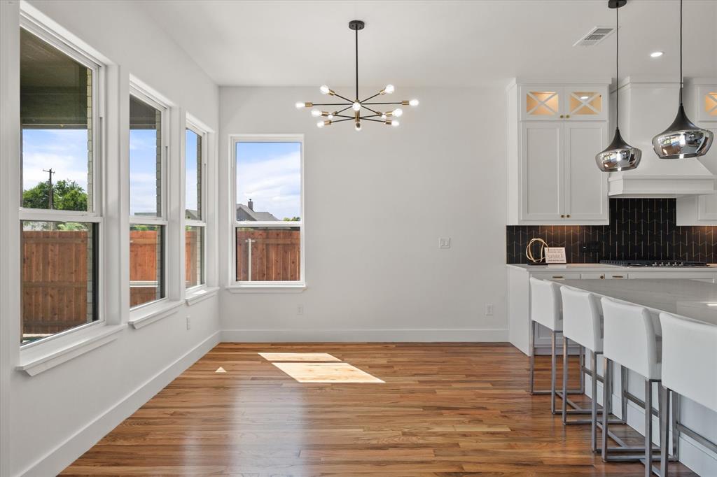 Open-concept space featuring wood-finish flooring, a modern multi-arm chandelier, white shaker-sty
