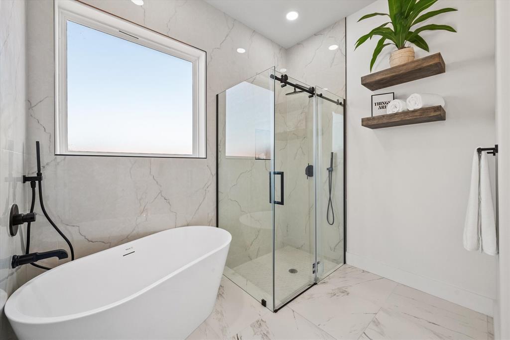 Freestanding soaking tub with matte black fixtures, glass-enclosed shower with matte black hardware, lwall-mounted wood shelving