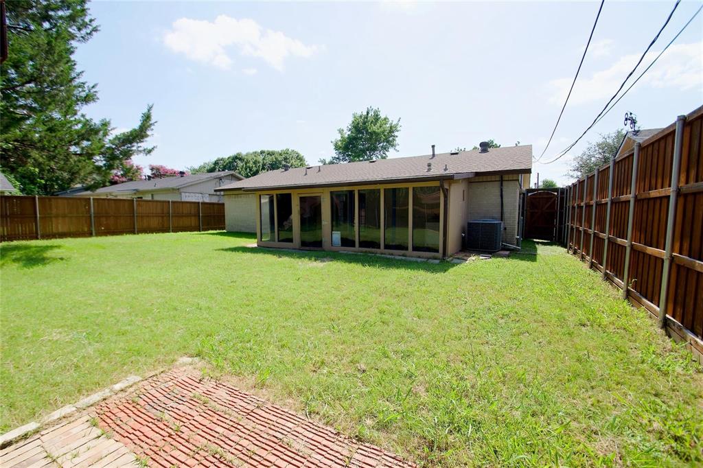 Backyard featuring a red brick patio, sprawling grass lawn, floor-to-ceiling glass paneling, and perimeter wood fencing