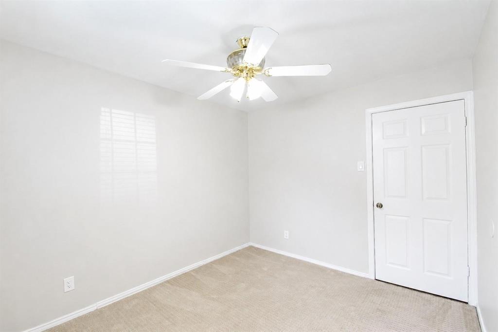 Neutral-toned interior space featuring wall-to-wall carpeting, a six-panel interior door, and a multi-light ceiling fan