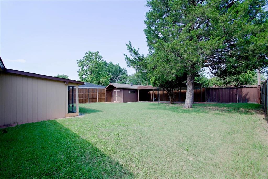 Expansive backyard featuring a level lawn, mature shade trees, a detached storage structure, and perimeter wood fencing
