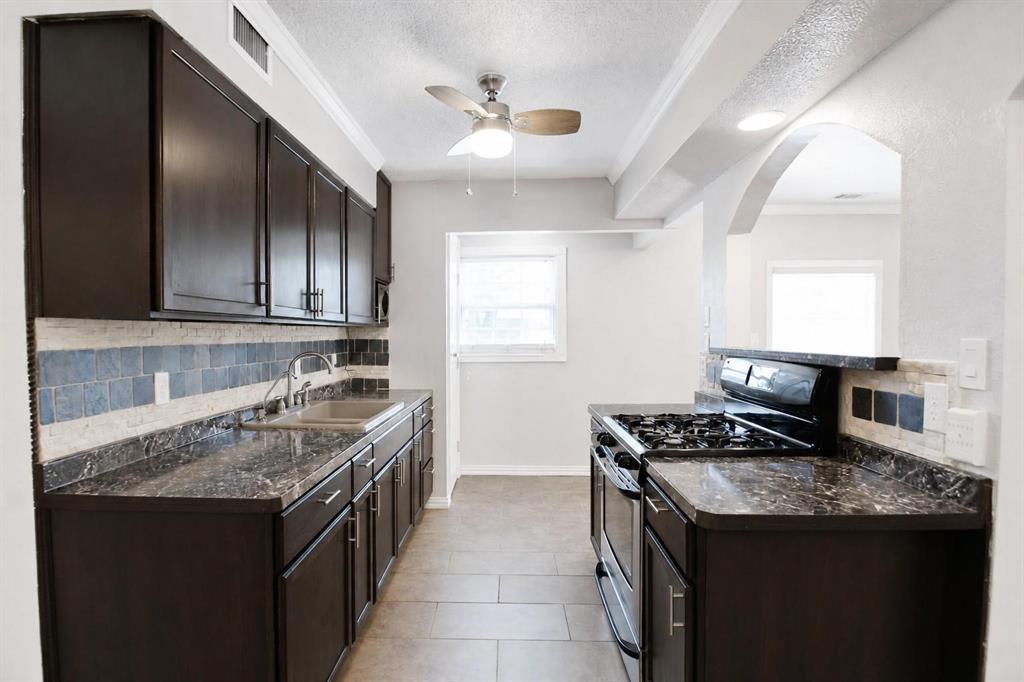 Kitchen featuring dark-finish cabinetry, patterned stone-surface countertops, tile backsplash, tile flooring, and an arched architectural opening