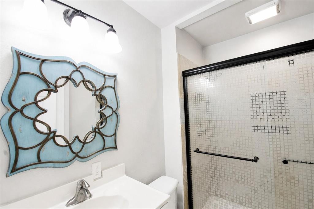 Bathroom vanity featuring a solid surface countertop with integrated basin, three-light wall fixture, and walk-in shower with a black-framed sliding door
