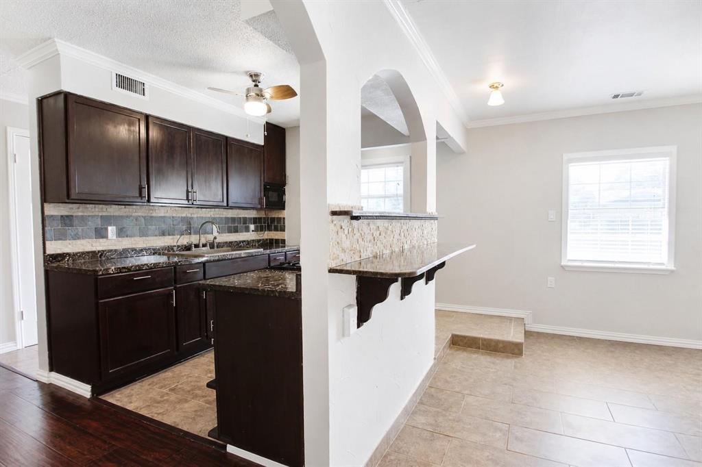 Kitchen featuring dark cabinetry, stone-surface countertops, stone tile backsplash, breakfast bar with stone veneer detailing, and arched wall opening
