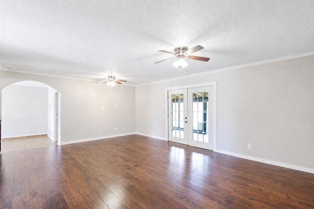 Spacious interior featuring wood-finish flooring, dual ceiling fans with integrated lighting, a structural arched doorway, and double-paned glass French doors Spacious interior featuring wood-finish flooring, dual ceiling fans with integrated lighting, a structural arched doorway, and double-paned glass French doors