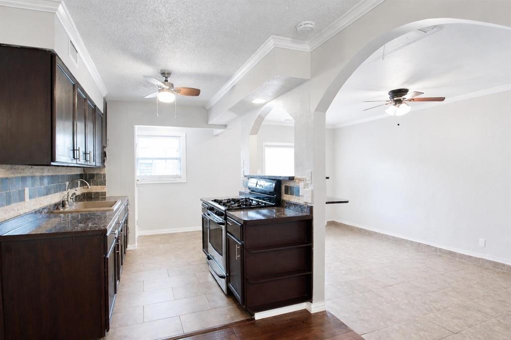 Kitchen featuring dark cabinetry, stone-finish countertops, tiled backsplash, stainless steel gas range, and arched architectural detailing