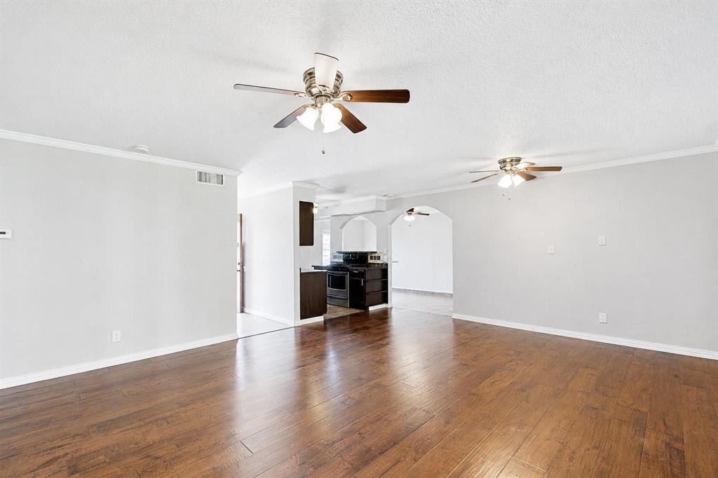 Wood-finish flooring, dual ceiling fans with integrated lighting, neutral wall paint, and architectural arched doorways