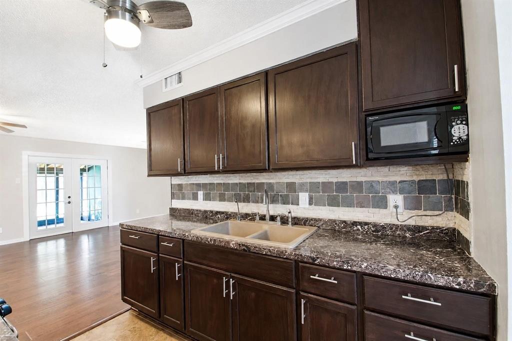 Kitchen featuring dark-finish cabinetry, stone-patterned countertops, a dual-basin sink, multi-tone tile backsplash, and a built-in microwave