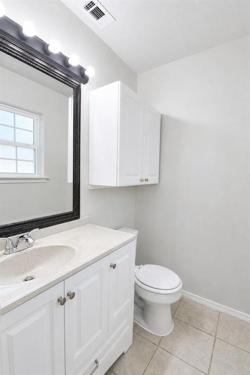 Bathroom featuring white cabinetry, solid-surface countertop with an integrated sink, wall-mounted storage cabinet, framed mirror with integrated lighting, and tile flooring