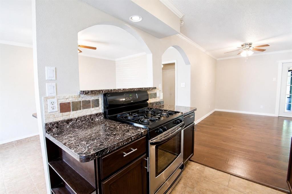 Kitchen featuring dark wood-finish cabinetry, a gas range, stone-patterned countertops, decorative tile backsplash, and arched wall openings