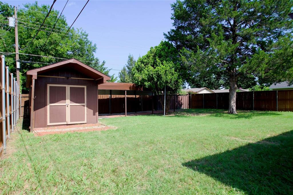 Rear yard featuring a manicured lawn, detached storage shed, covered outdoor structure, wood-style perimeter fencing, and mature trees