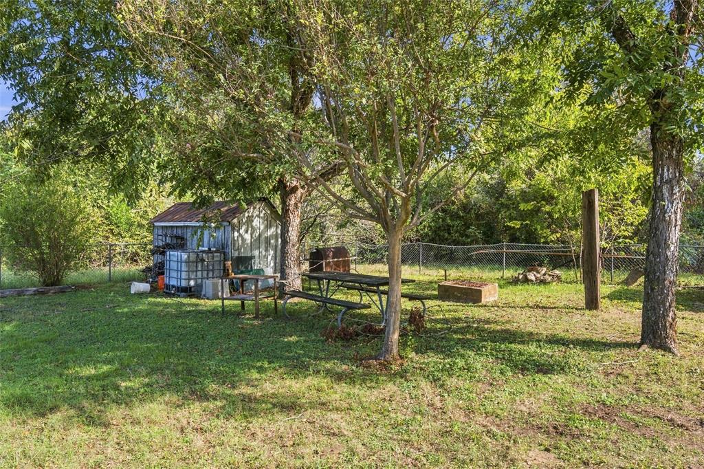 Spacious backyard featuring mature trees, a detached storage structure, and chain-link perimeter fencing
