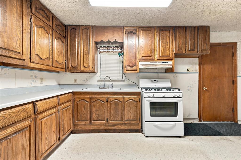 Kitchen featuring raised-panel wood cabinetry, white countertops, integrated sink with metal faucet, and white freestanding gas range