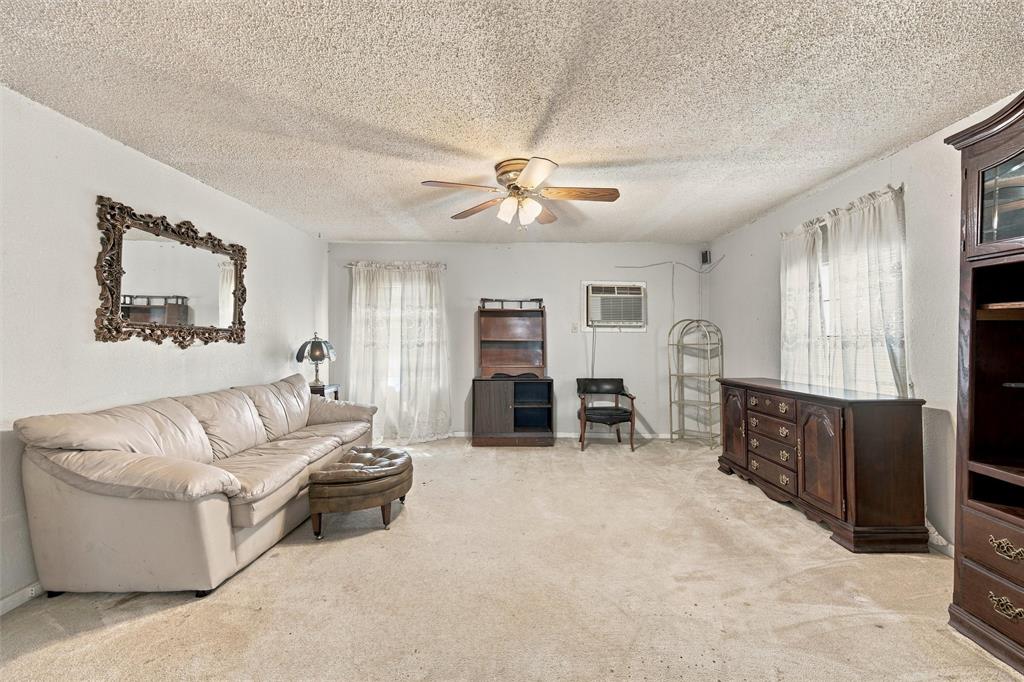 Living area featuring a textured ceiling, neutral wall tones, carpeted flooring, and a central ceiling fan with integrated lighting