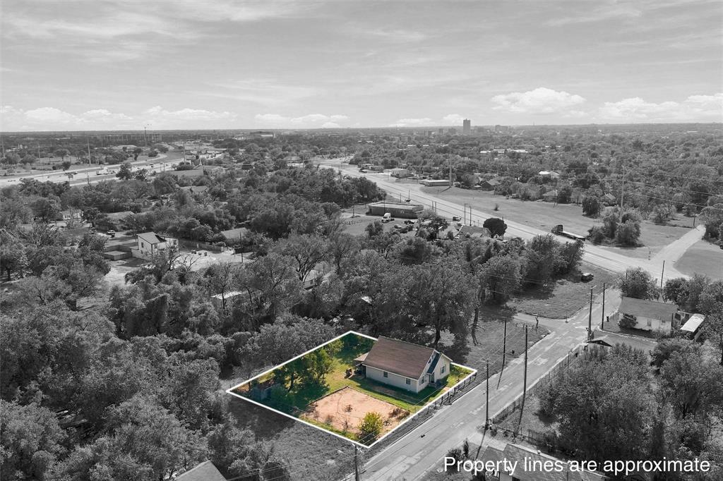 Aerial perspective of a corner lot featuring a single-story residence, mature trees, and an open ground area
