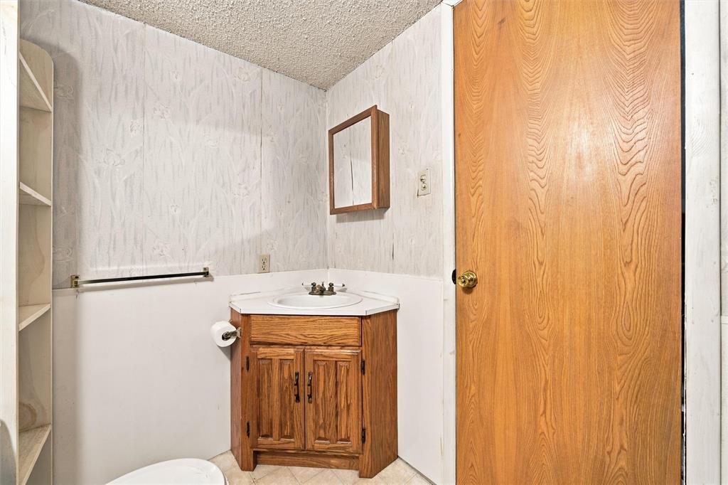Corner vanity with wood-finish cabinetry, inset sink, and built-in shelving, complemented by a wall-mounted medicine cabinet and solid wood-finish door